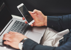 Eine Person benutzt ein Smartphone und einen Laptop gleichzeitig, möglicherweise in der Deinstallation von Apps beschäftigt.